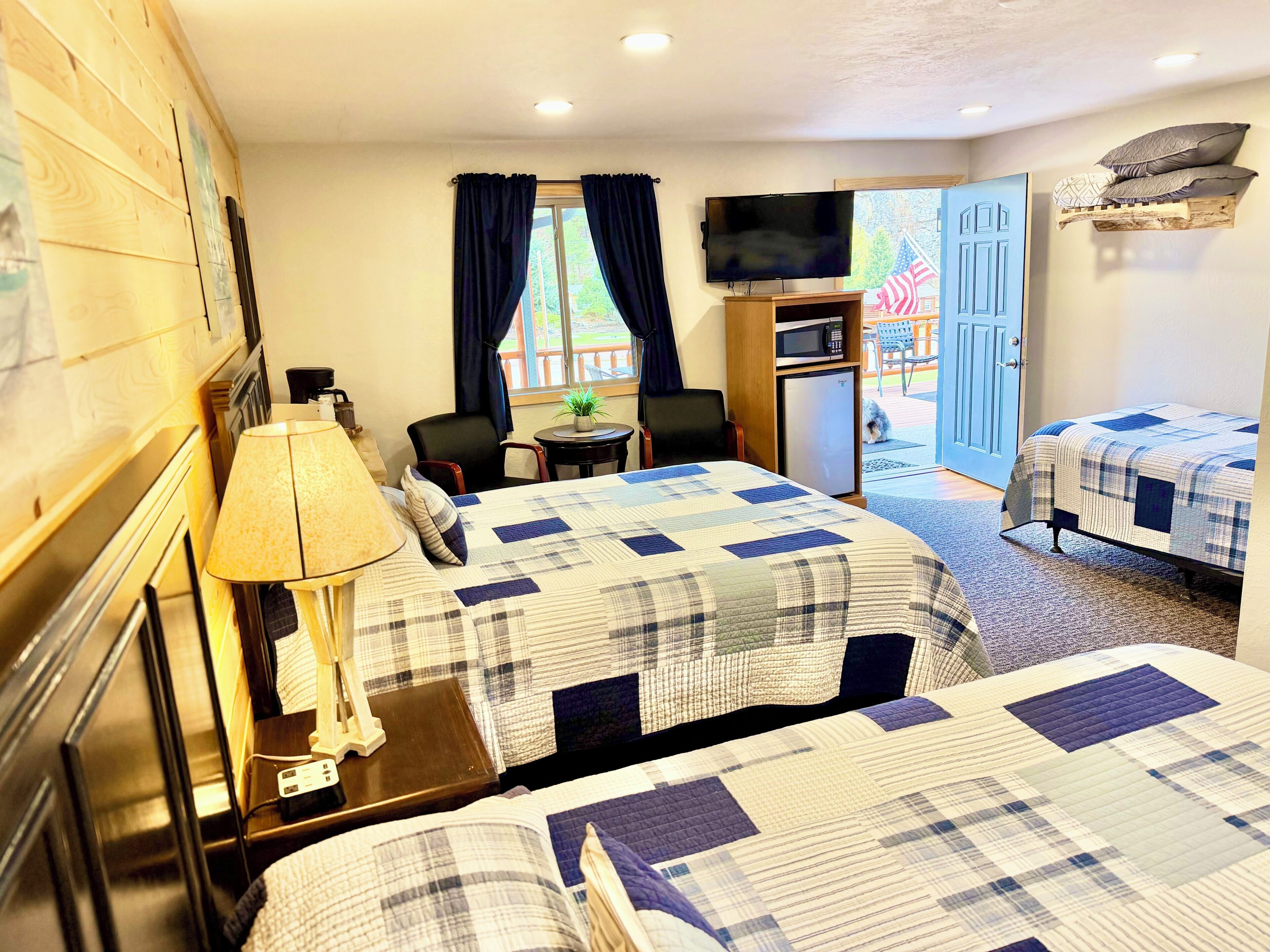 A hotel room with two beds, a TV, a desk with a computer, a chair, and a small table with a plant.