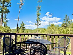 A deck with a table and chairs, overlooking a forested area with hills. - Mountain View Lodge & Cabins (Rapid City)