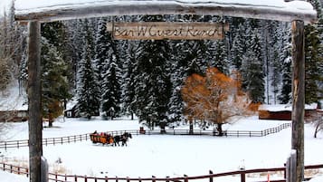Un cartello di legno con su scritto 'Bar W Guest Ranch', immerso in un paesaggio innevato con una recinzione in legno e alberi.