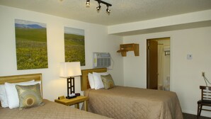 A hotel room with two beds, a nightstand with a lamp, a wooden chair, and a painting of a landscape on the wall. - Trout Montana Motel (Cascade)
