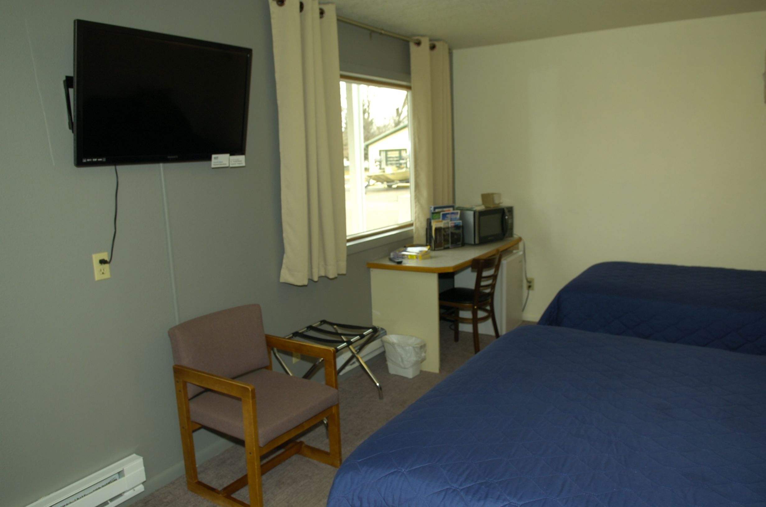 A room with a bed, a desk with a computer and a TV, a chair, and a window with curtains.
