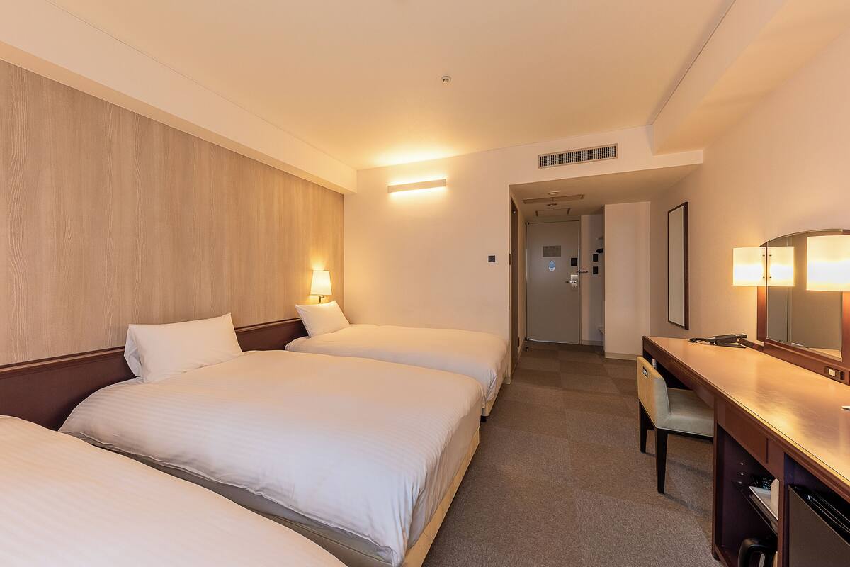 Une chambre d’hôtel avec deux lits, un bureau, une chaise, une lampe et un miroir.