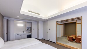 Hotelkamer met een groot bed, een bureau met stoel, een spiegel en een schuifdeur naar een zithoek.