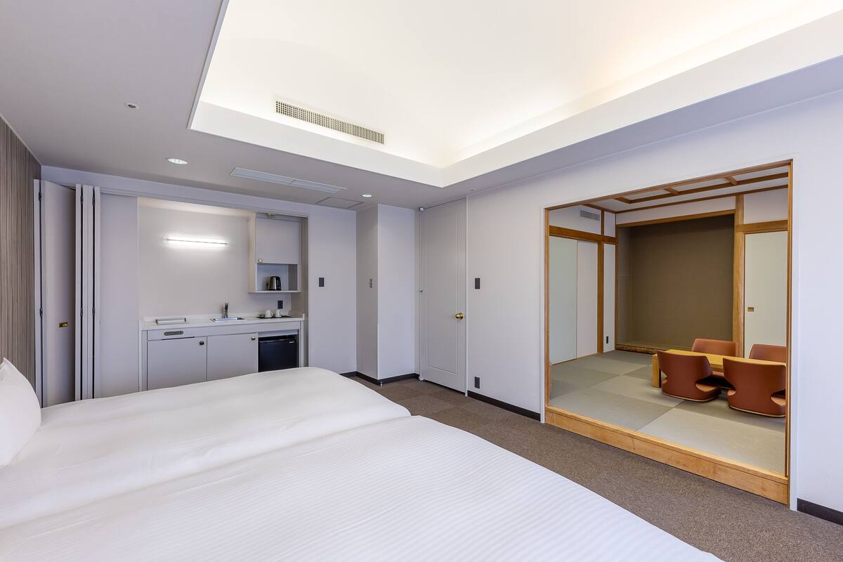 Une chambre d’hôtel avec un grand lit, un bureau avec une chaise, un miroir et une porte coulissante donnant sur un coin salon.