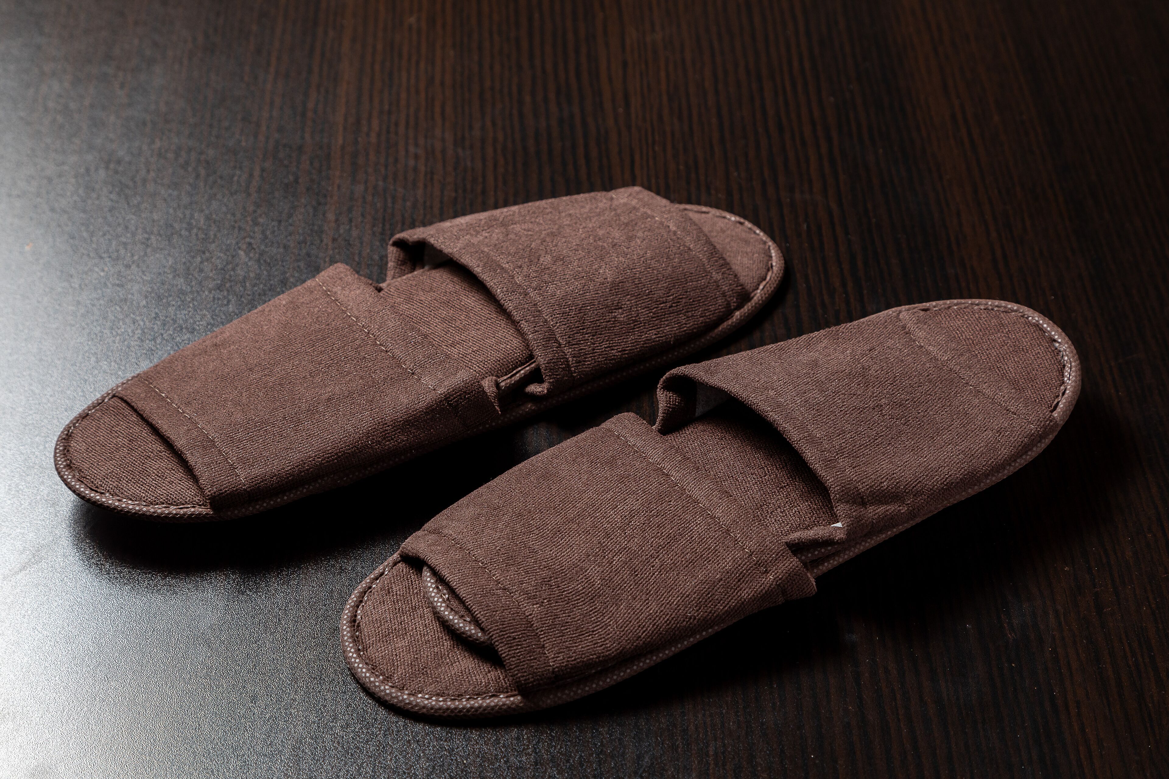 A pair of brown slippers on a dark wooden surface.