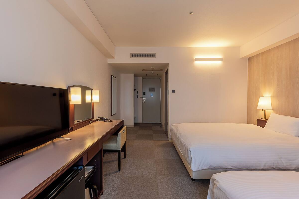 Une chambre d’hôtel avec un lit, un bureau, une chaise, une télévision et une porte de salle de bain.