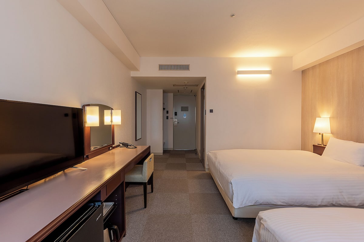 A hotel room with a bed, a desk, a chair, a television, and a bathroom door.