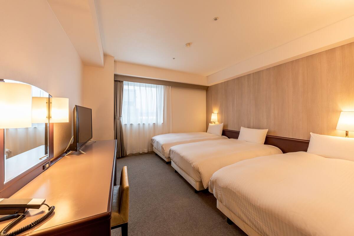 Une chambre d’hôtel avec deux lits, un bureau avec une chaise, une télévision et une lampe.