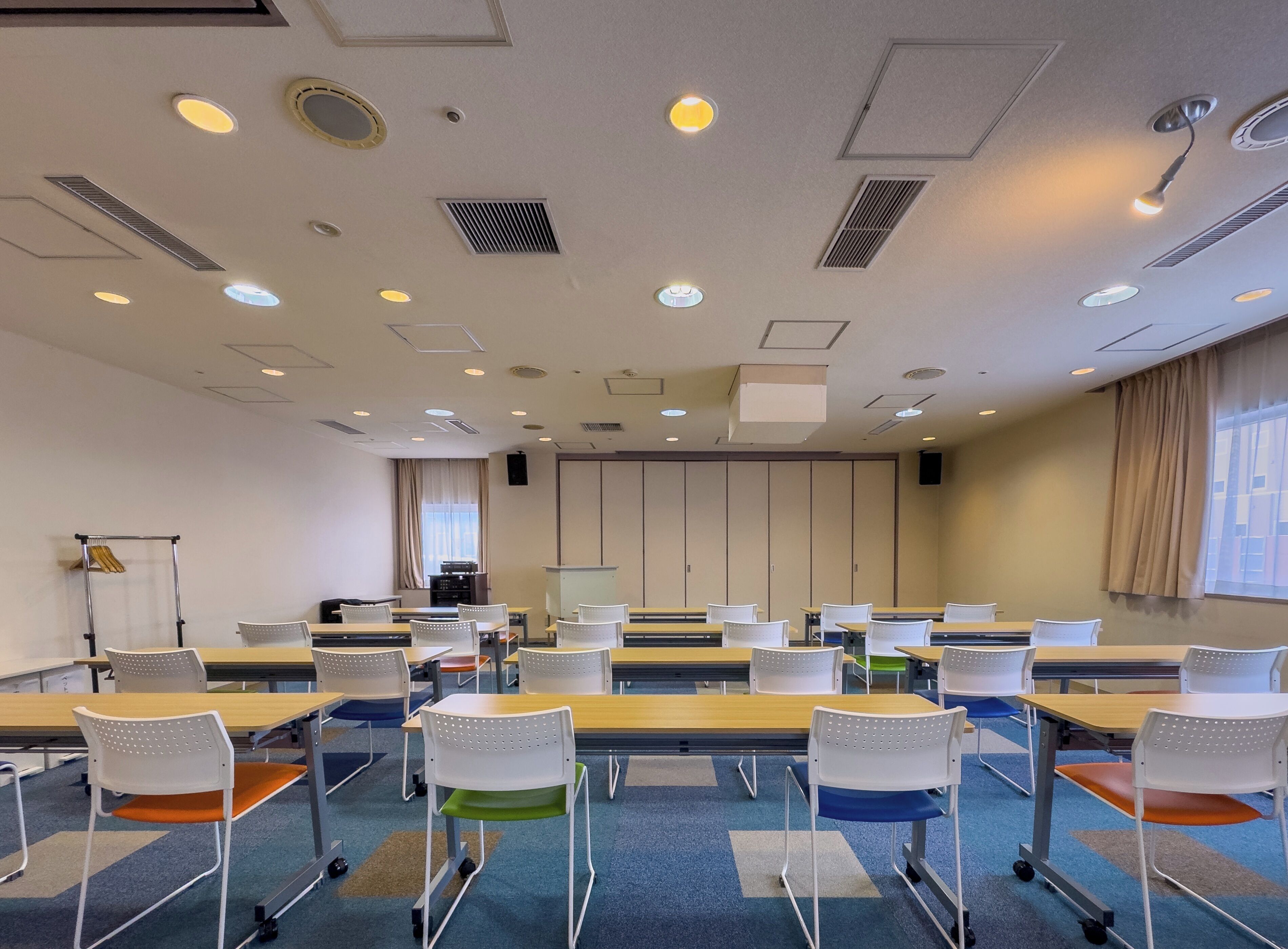 A conference room with tables, chairs, ceiling lights, and a projector screen.