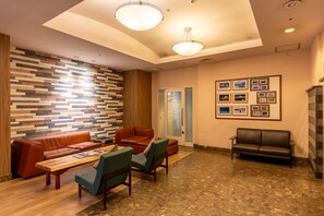 Eine moderne Lobby mit einer Holzvertäfelung, einem braunen Ledersofa, grünen Sesseln, einem Holztisch und gerahmten Bildern an der Wand.