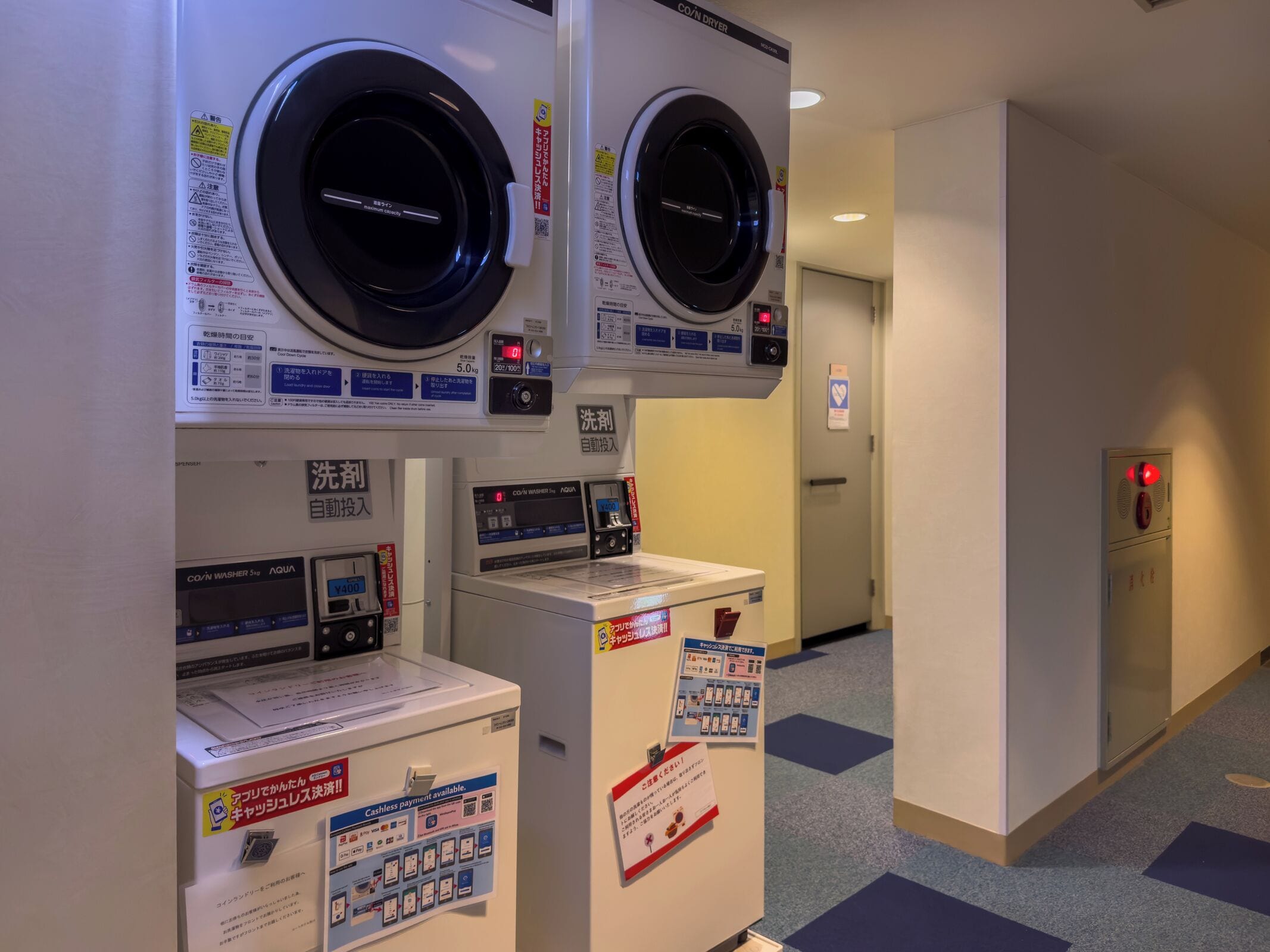 A laundry facility with multiple washing machines, a payment terminal, and a fire alarm.