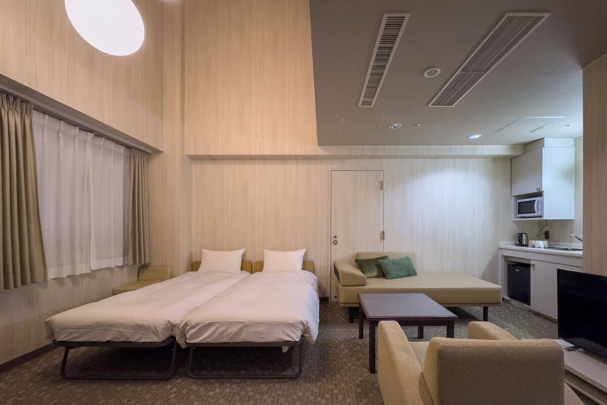 Une chambre d’hôtel avec un lit double, un canapé, une petite table, une télévision et une kitchenette.