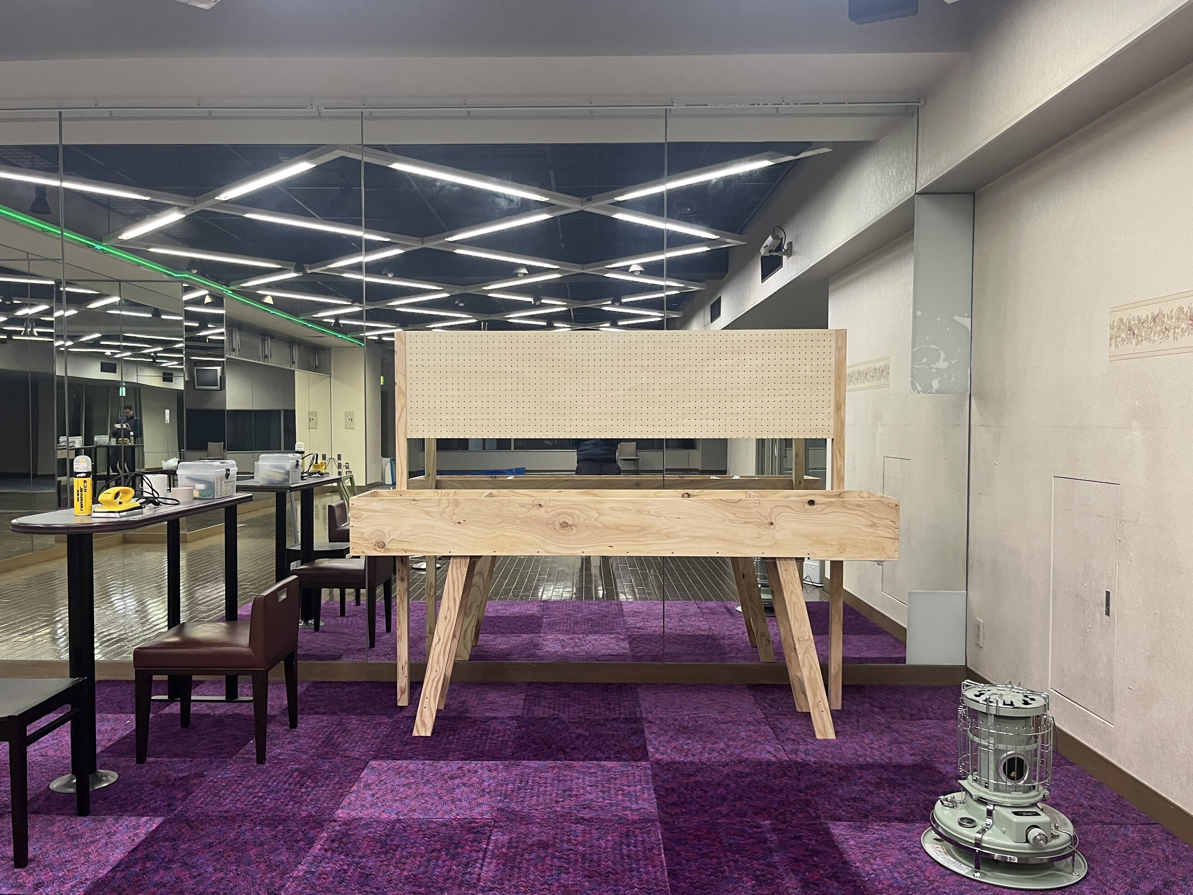 Een moderne kantoorruimte met een houten werkbank, paars tapijt en een plafond met lineaire verlichting.