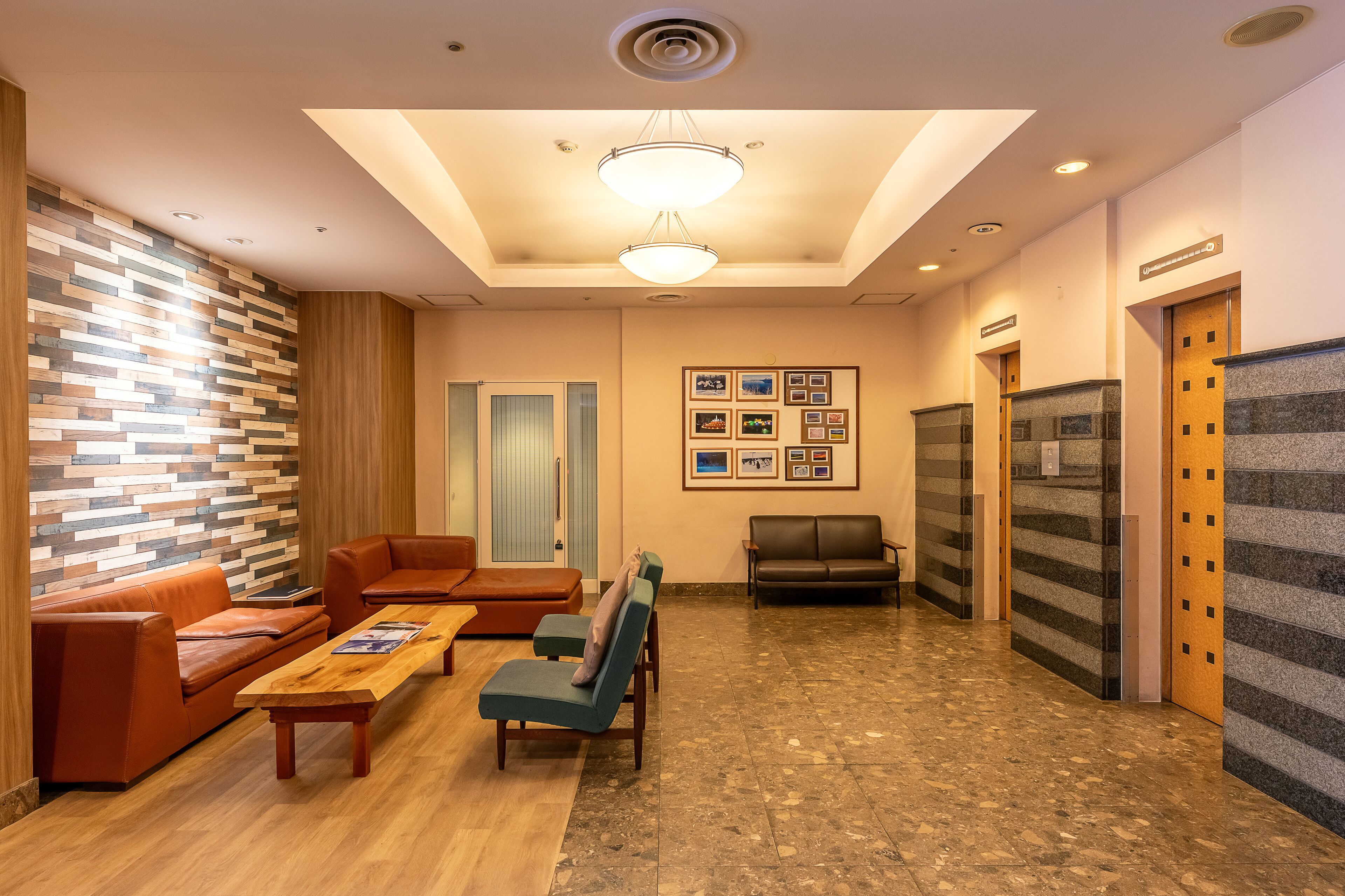 A lobby with a wooden floor, a seating area with sofas and chairs, a coffee table, and a wall with framed pictures.