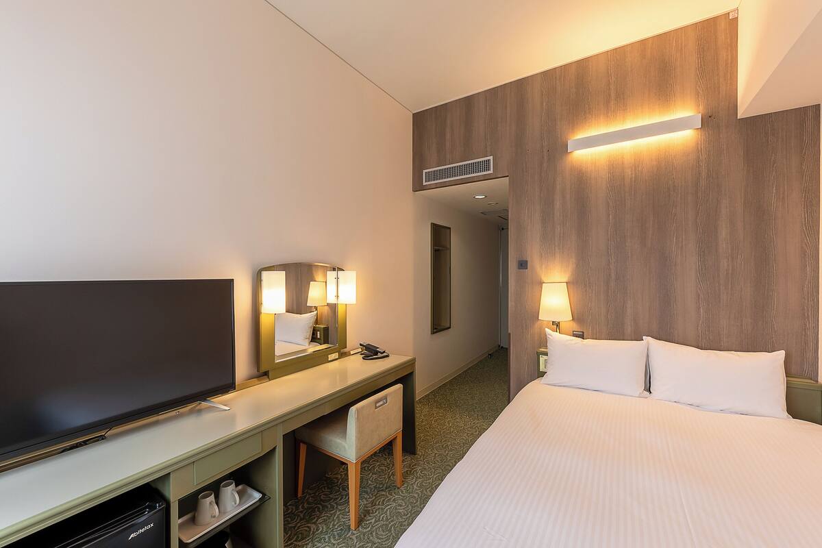 Une chambre d’hôtel comprenant un lit, un bureau avec une chaise, une télévision et un miroir.