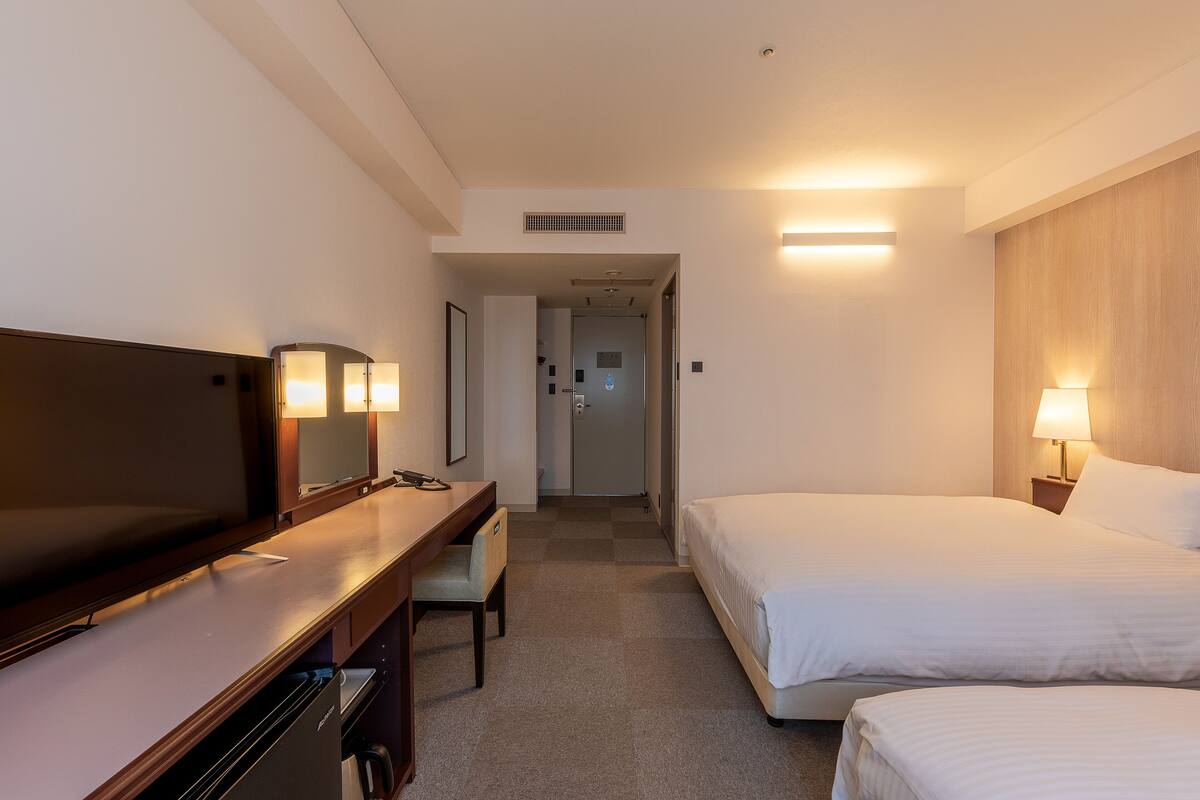 Une chambre d’hôtel avec un lit, un bureau et une chaise, une télévision et une lampe.