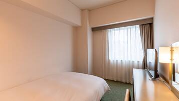 Una habitació d'hotel amb llit, escriptori amb làmpada i finestra amb cortines.