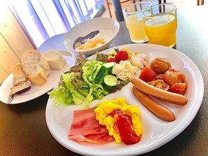 Ein Teller mit Eiern, Schinken, Ketchup, Würstchen und einem Beilagensalat.