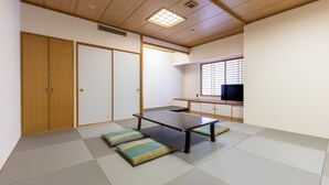 Een traditionele Japanse kamer met tatami vloeren, een lage tafel, kussens, schuifdeuren en een televisietoestel.
