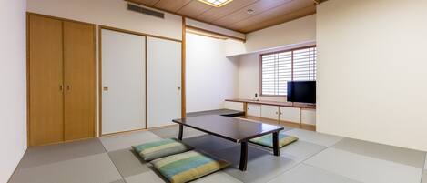 Una habitación japonesa tradicional con suelo de tatami, una mesa baja, cojines, puertas correderas y una televisión.