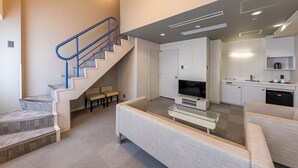 Een moderne woonkamer met een trap, een flatscreen televisie en een keukenhoek.