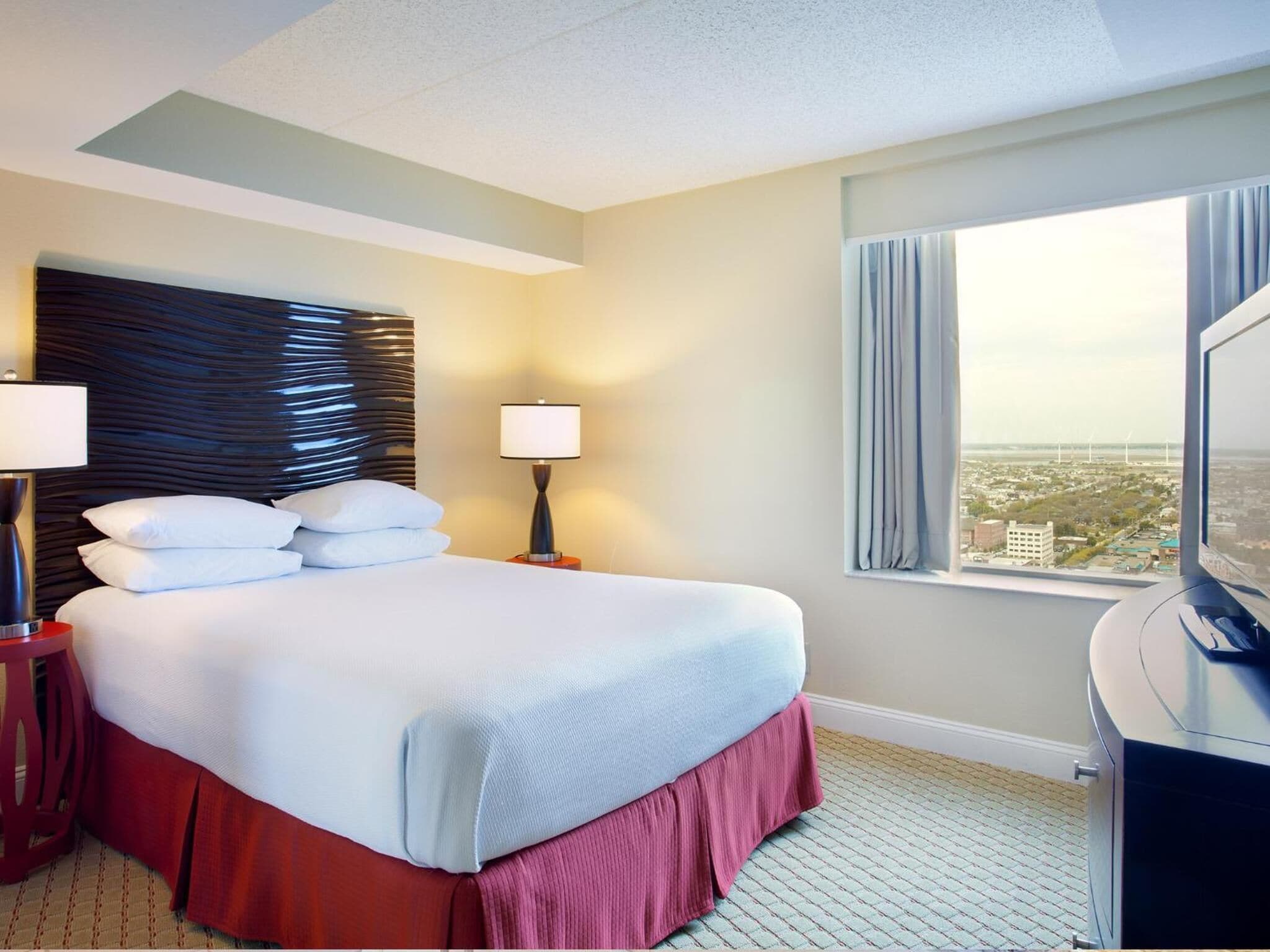A hotel room with a large bed, two bedside lamps, a TV, and a window with a city view.