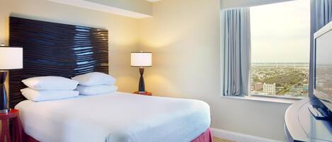 A hotel room with a large bed, two bedside lamps, a TV, and a window with a city view.