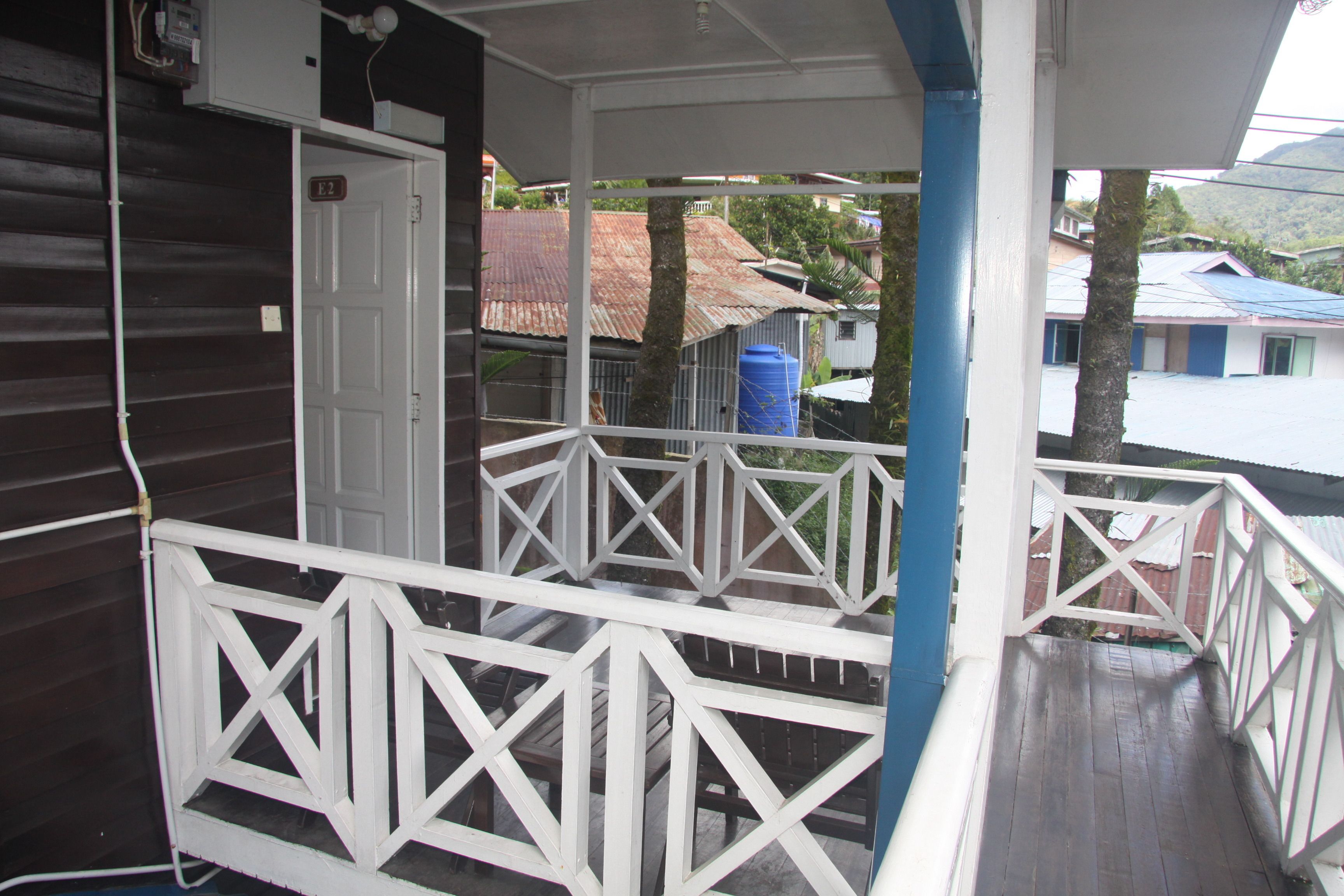 A wooden building with a balcony, a door labeled 'E2', and a blue water tank in the background.