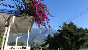 A building with a covered porch, a hanging flower arrangement, and a mountain view in the background. - Kinabalu Pine Resorts (Ranau)