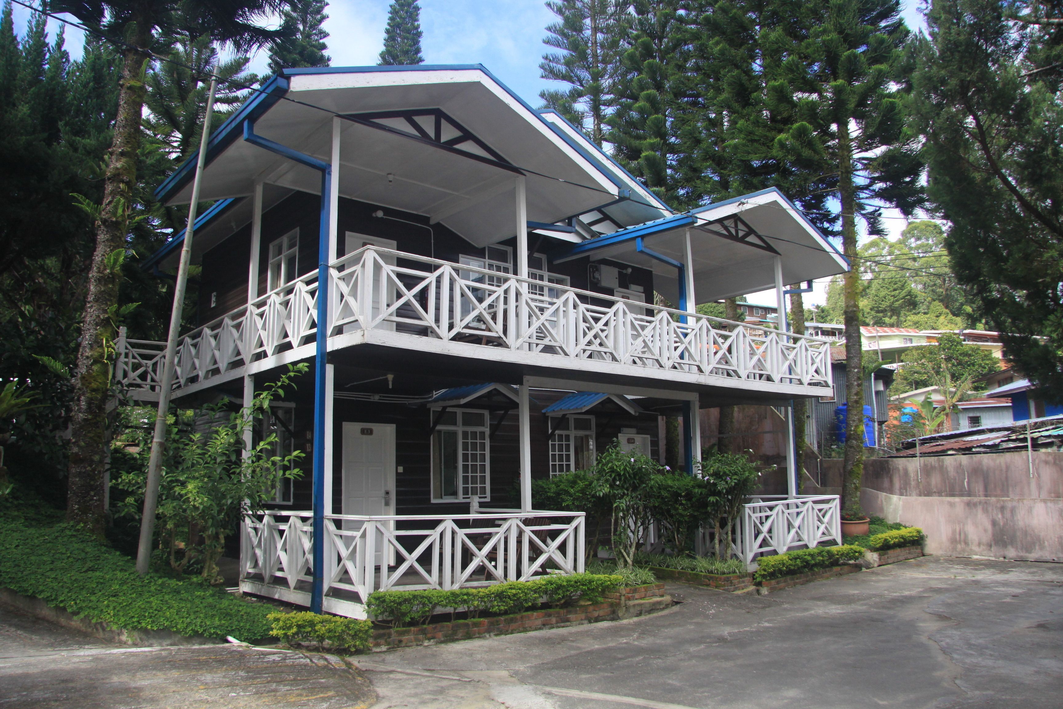 A two-story building with a balcony on the upper floor, surrounded by greenery.