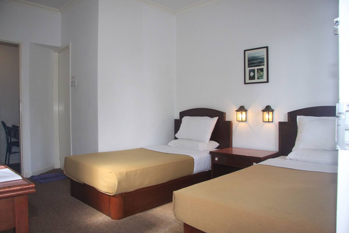 Ein Hotelzimmer mit zwei Einzelbetten, einem Schreibtisch und einem Stuhl.