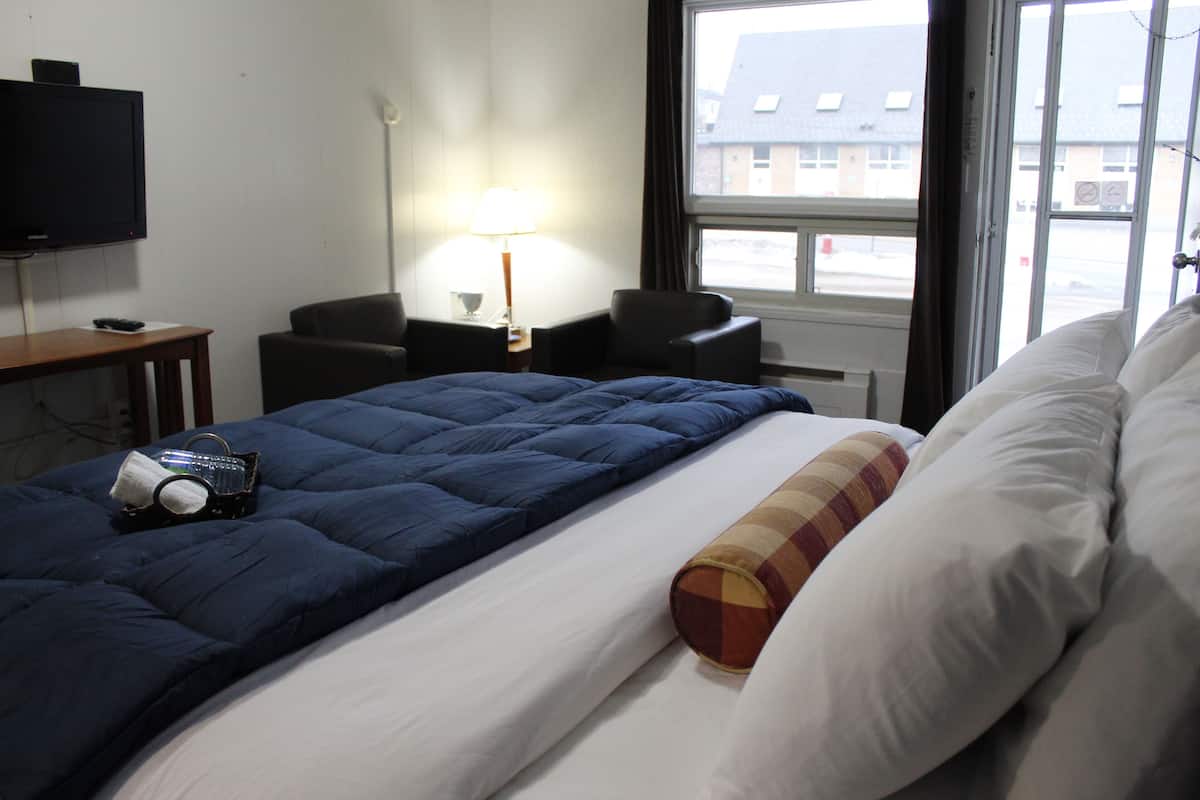Una habitación de hotel con cama, escritorio con lámpara, silla y televisor en la pared.