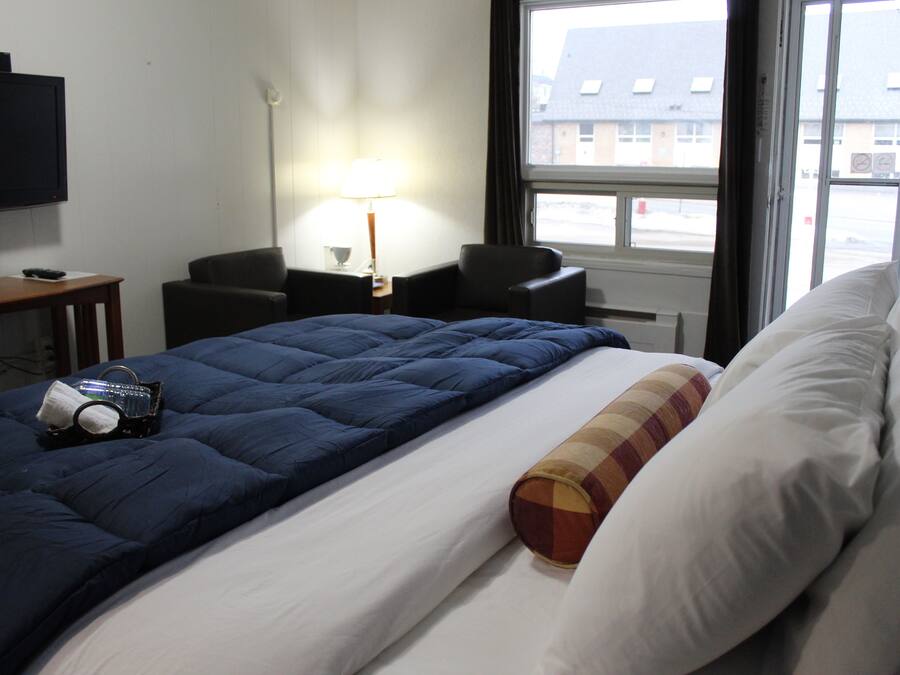 Quarto de hotel com cama, escrivaninha com luminária, cadeira e televisão na parede.