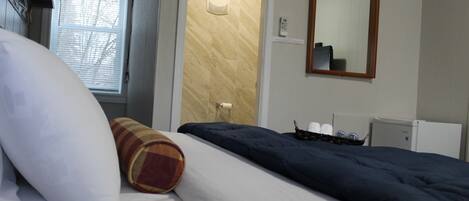 A hotel room with a bed, a window with blinds, a door, a mirror, and a radiator.