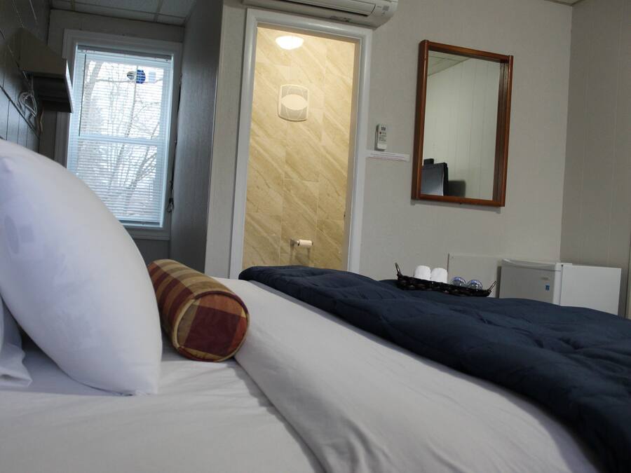 Una habitación de hotel con cama, ventana con persianas, puerta, espejo y radiador.