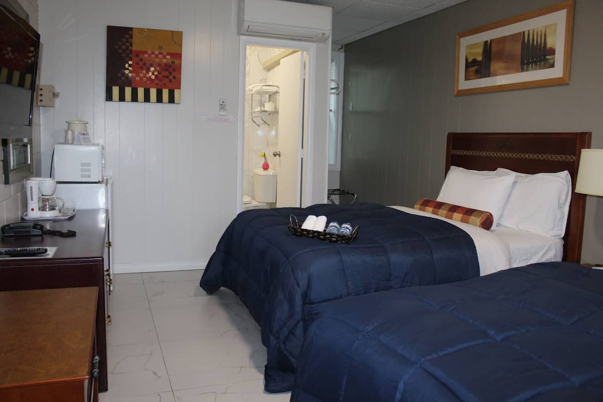 Habitación de hotel con dos camas, un escritorio con teléfono y cafetera, y un baño visible a través de una puerta abierta.