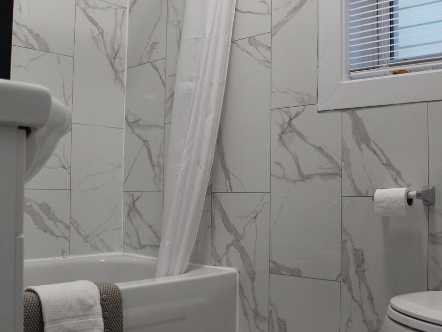Une salle de bain avec une baignoire, des toilettes et une fenêtre avec des stores.