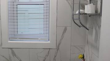 A bathroom with a toilet, a window with blinds, a towel rack, and a vase with flowers.