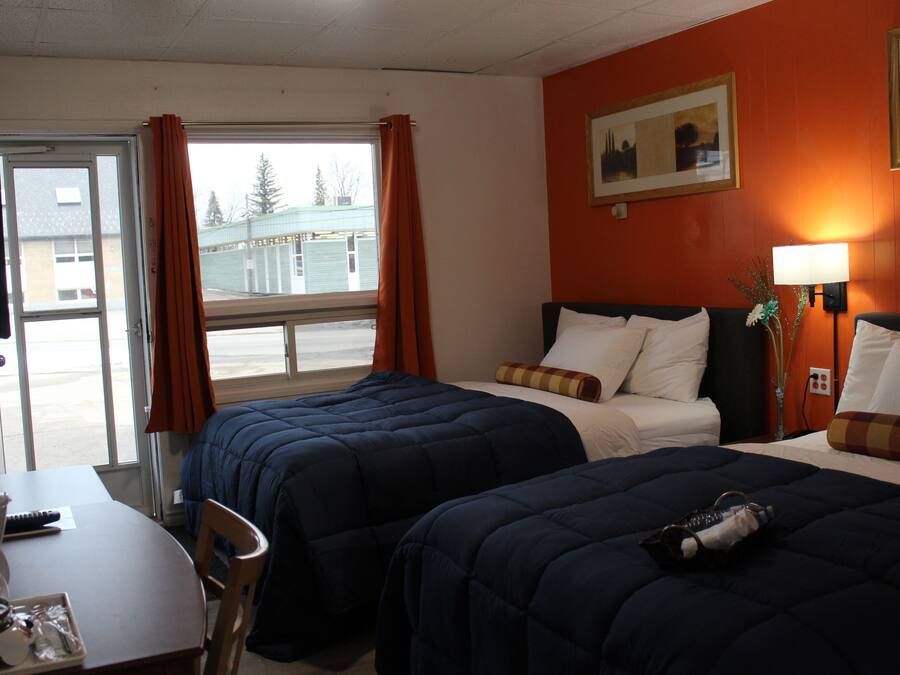 Una habitación de hotel con dos camas, una mesa con una silla y un ventanal con cortinas.
