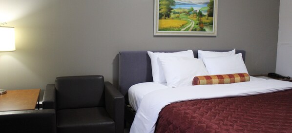 A hotel room with a bed, a desk, a chair, and a painting on the wall. - Sunrise Inn (Parry Sound)