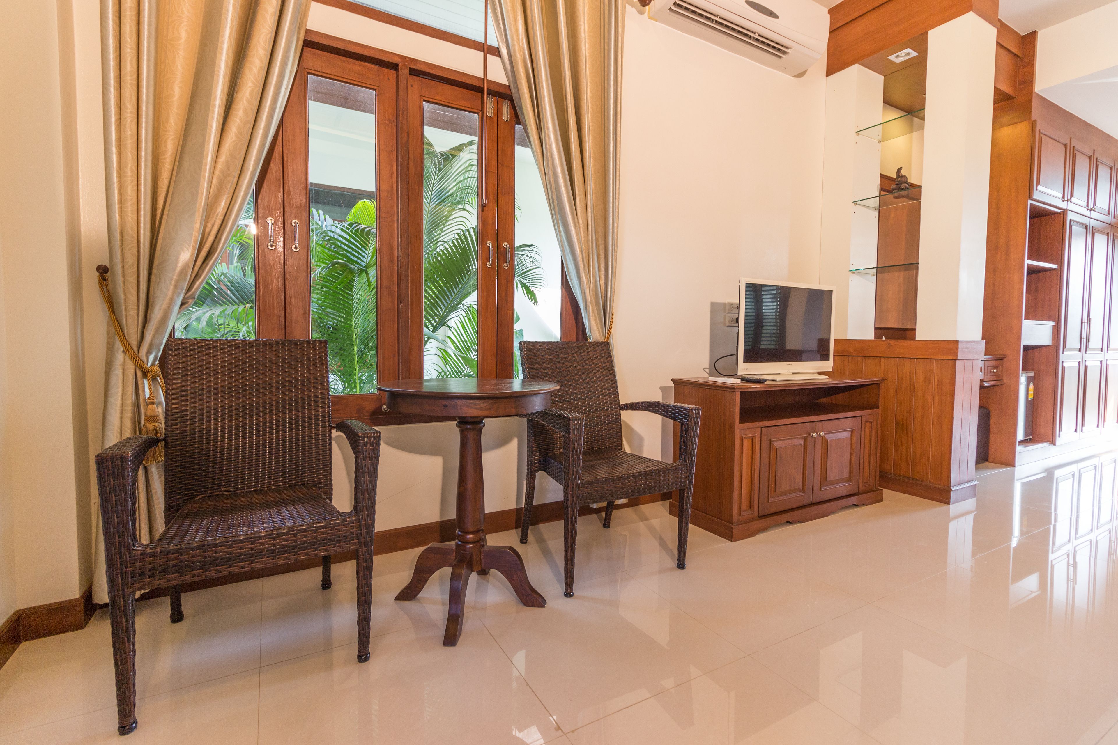 A room with a wooden cabinet, a television, wicker chairs, and a table.