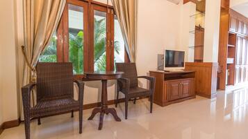 A room with a wooden cabinet, a television, wicker chairs, and a table.