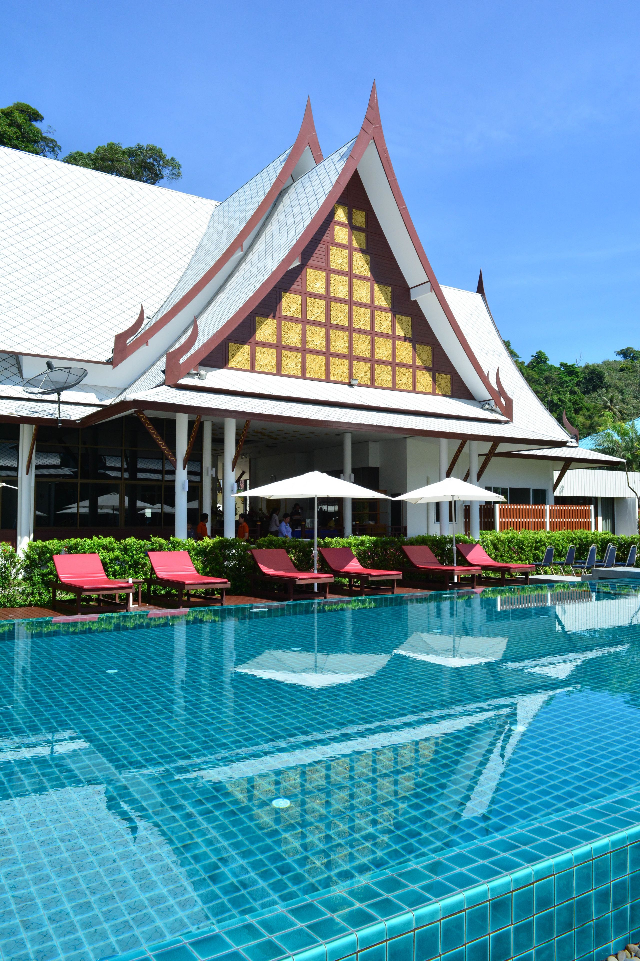 Ein Hotel mit Schwimmbad, roten Liegestühlen und traditioneller Architektur.