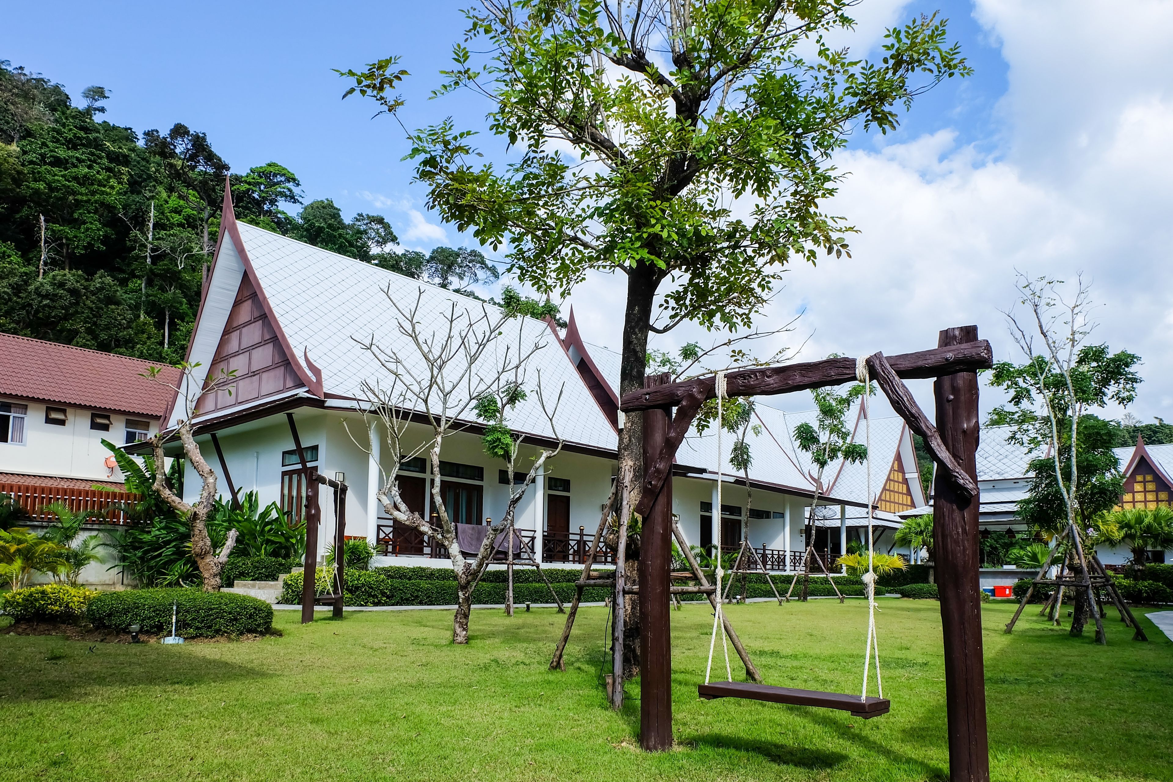 A traditional building with a sloped roof, surrounded by a well-maintained garden with swings and trees.