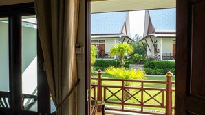 Uitzicht vanuit een kamer met een houten deur die leidt naar een balkon met houten balustrade en een klein tuintje met planten.