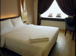 A neatly made bed with a folded towel, a bedside table, and a chair.