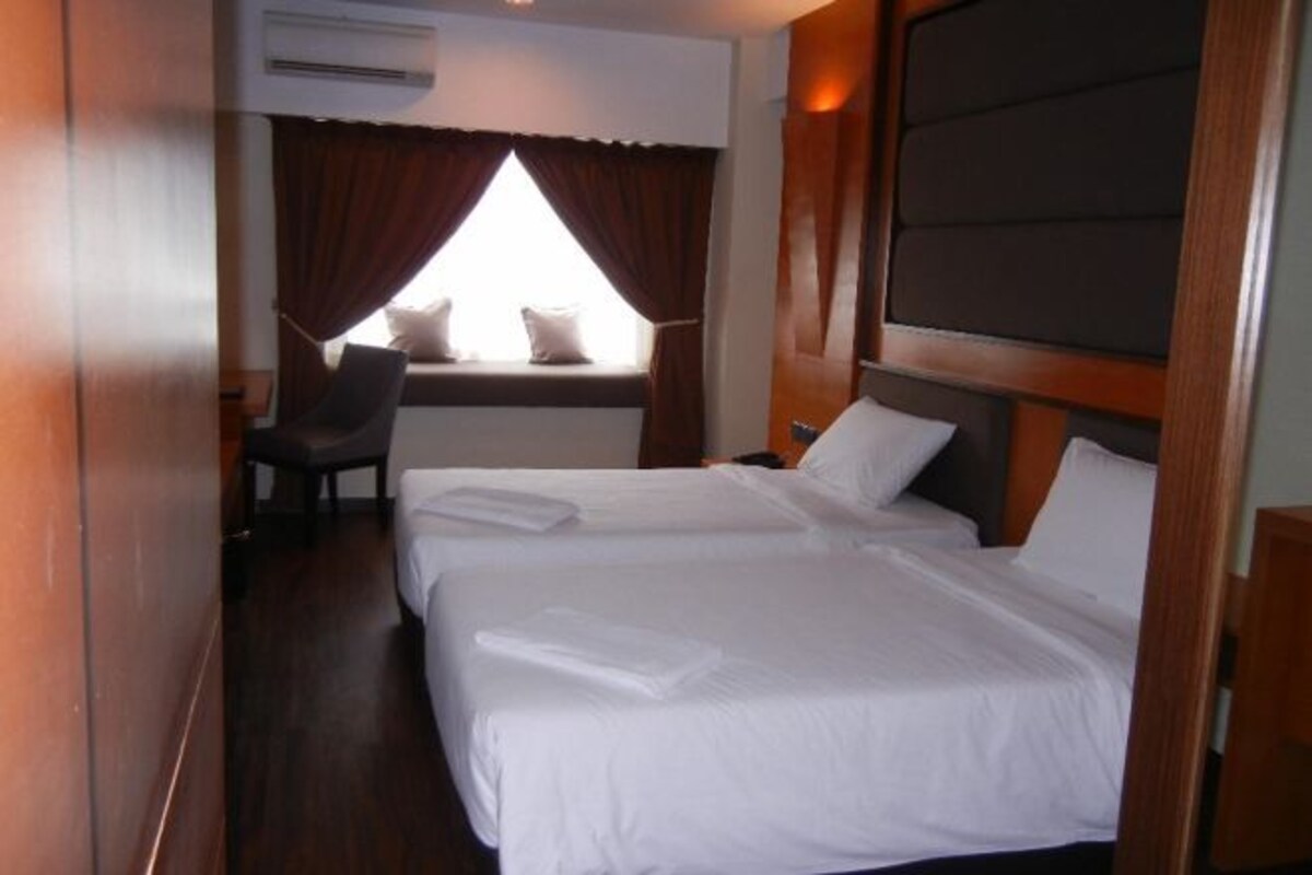 A hotel room with two beds, a window with curtains, a chair, and a wooden headboard.