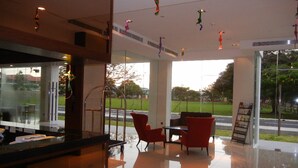 A modern interior with a reception desk, red chairs, and large windows offering a view of a park and road. - C'haya Hotel (Kota Kinabalu)