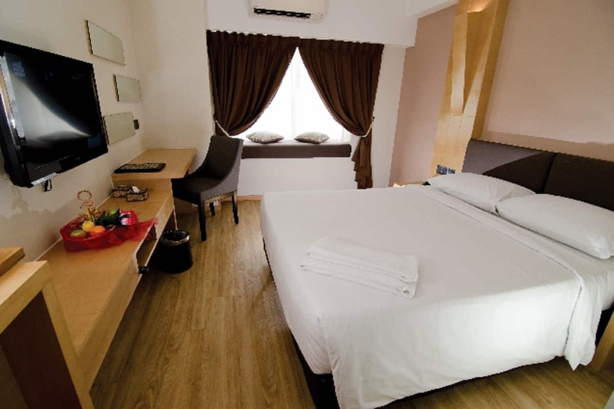 A hotel room with a bed, a desk with a computer, a TV, and a window with curtains.