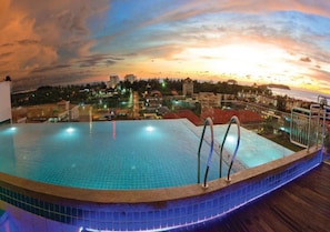A swimming pool with a tiled edge, a metal ladder, and a view of a cityscape at sunset.